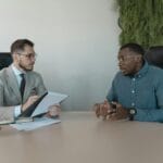 Jak wspólnie z agencją pracy planować rekrutacje pod sezon i szczyty produkcji Dwóch biznesmenów omawia rekrutację sezonową w nowoczesnym biurze