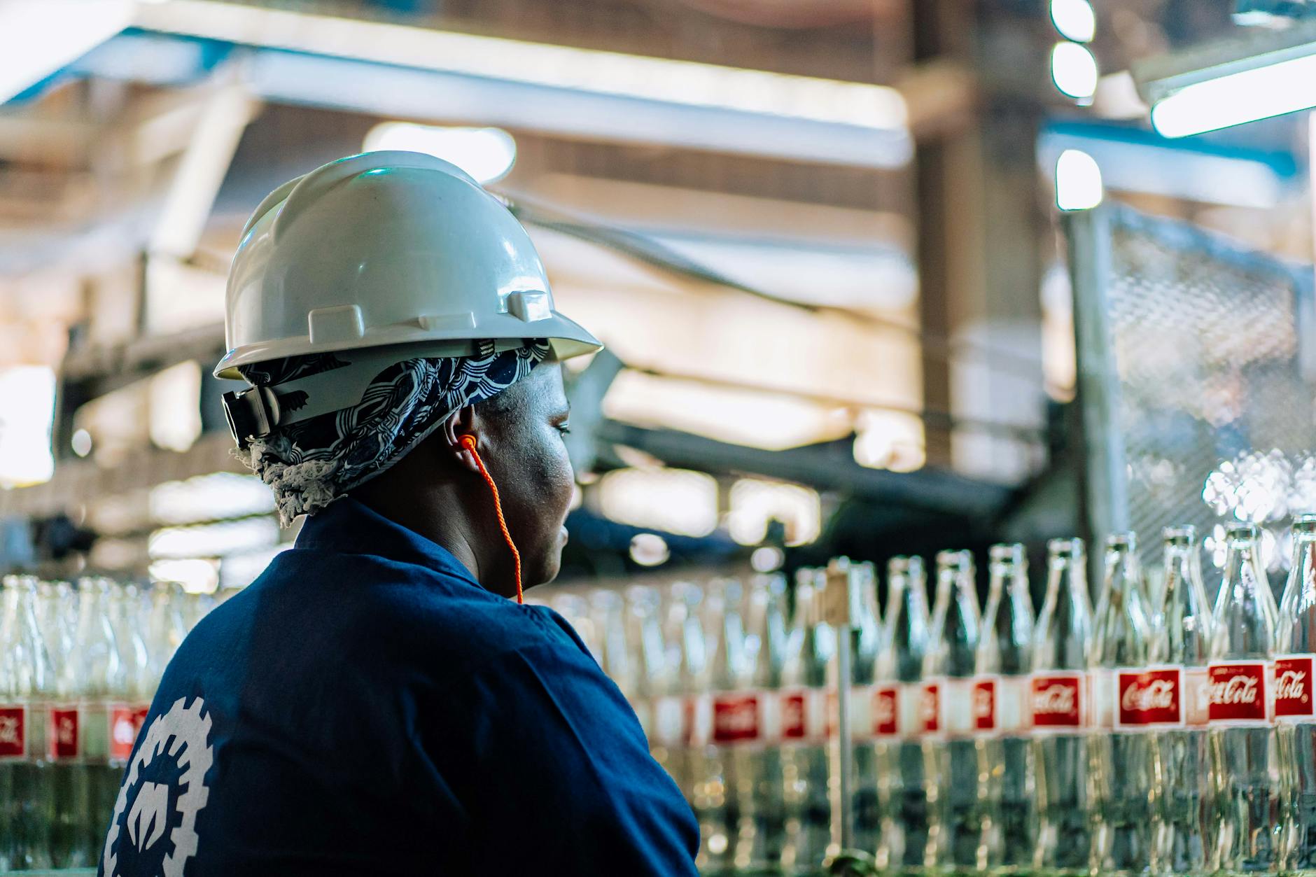 Jak wdrażać pracowników tymczasowych, by szybko osiągali wyniki na produkcji Pracownik w odzieży ochronnej kontroluje szklane butelki na produkcji