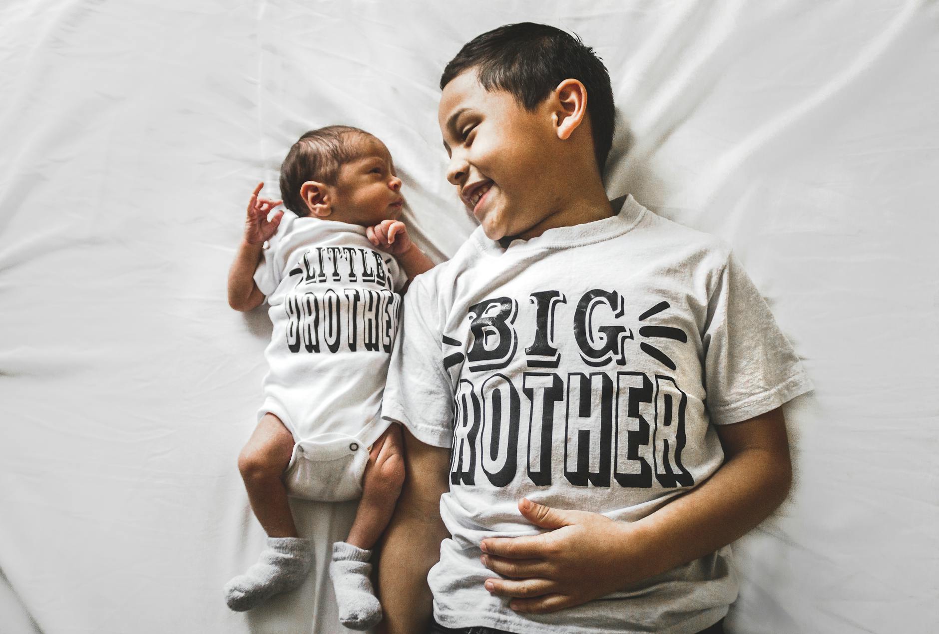 Starszy brat przytula noworodka, obaj w jednakowych koszulkach