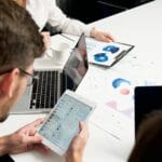 Jak zorganizować przepływ informacji między zmianami, działami i lokalizacjami firmy, by uniknąć błędów wynikających z niedomówień i niepełnego przekazania zadań Zespół w biurze omawia wykresy na laptopach i tabletach