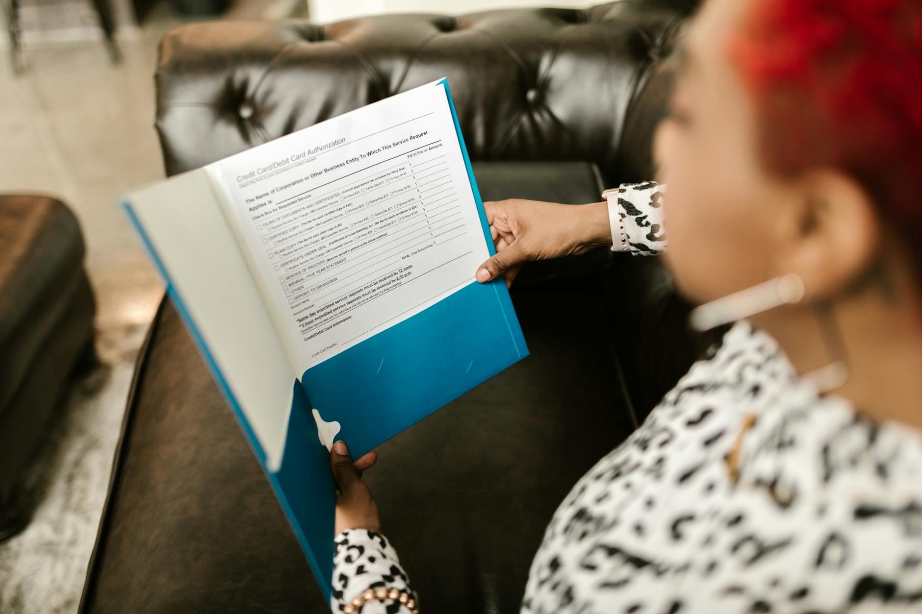 Kobieta na kanapie analizuje dokument w niebieskim folderze